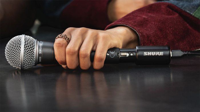 Shure MVX2U Gen 2 XLR to USB-C Audio Interface held by a person's handlaying across surface Shure MVX2U Gen 2 XLR to USB-C Audio Interface held by a person's hand laying across surface