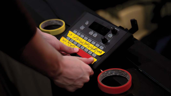 Person using red and yellow gaffer tape to label production console