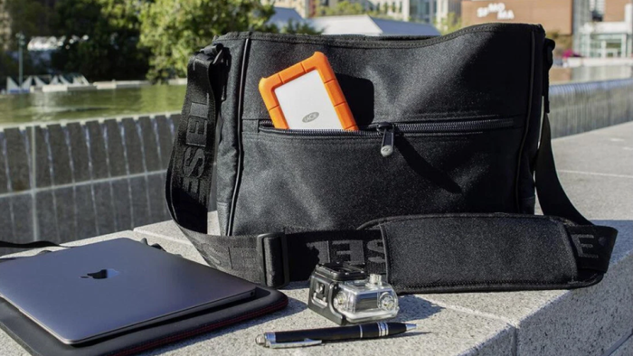 Laptop, pen, camera case, and portable SSD sticking out of a shoulder bag resting on the edge of a fountain