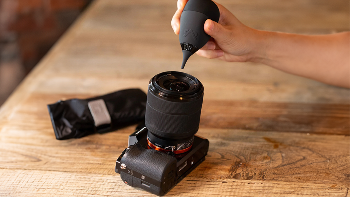 Person using air blower to clean dust off camera lens