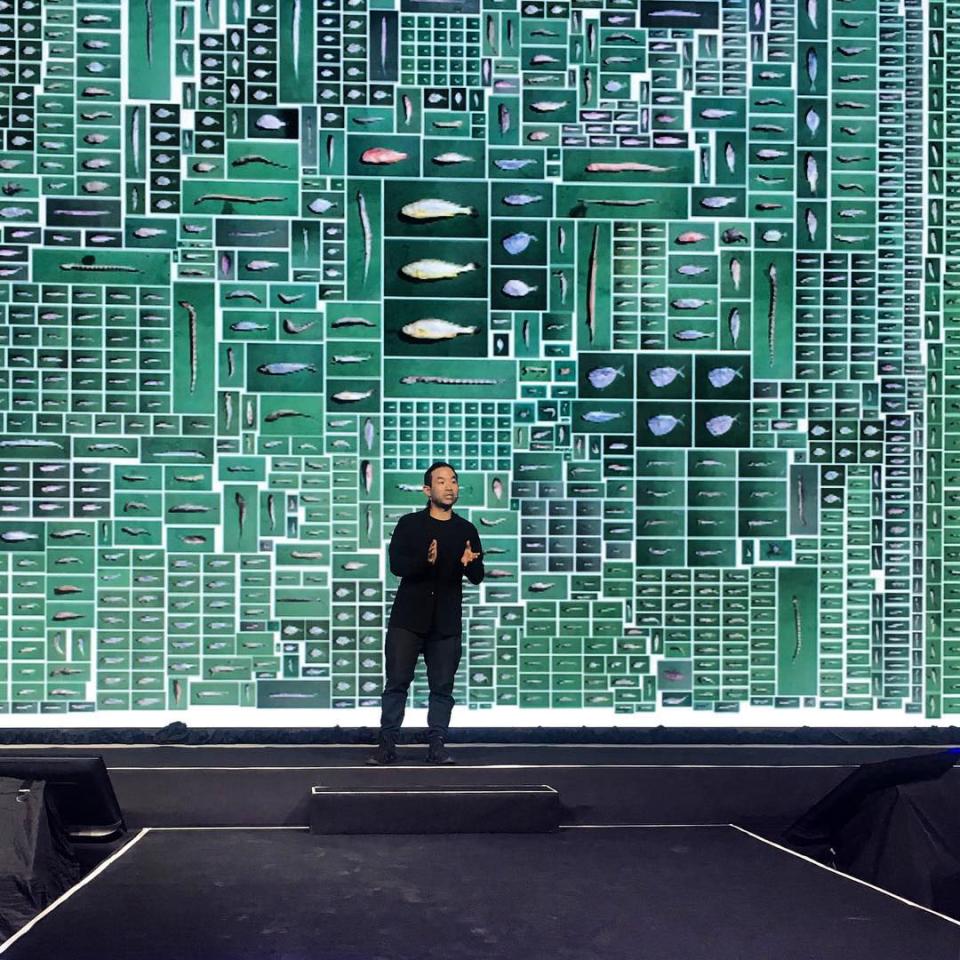 Chow speaks at an advertising conference with images from Chow and Lin’s work, “Equivalence—The Ecological Footprint of Fish” projected behind.