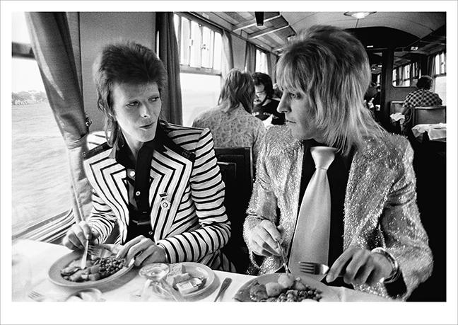 David Bowie and Mick Ronson on train to Aberdeen, 1973 © Mick Rock