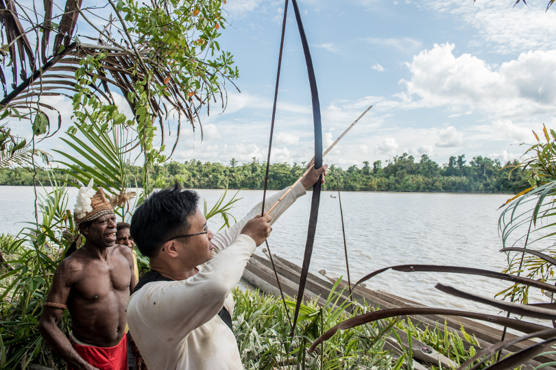 Joshua Irwandi tries a bow and arrow while in the field with Yakobus Sirarmbi, an Asmat elder. Image © Laurensius Reginaldus.