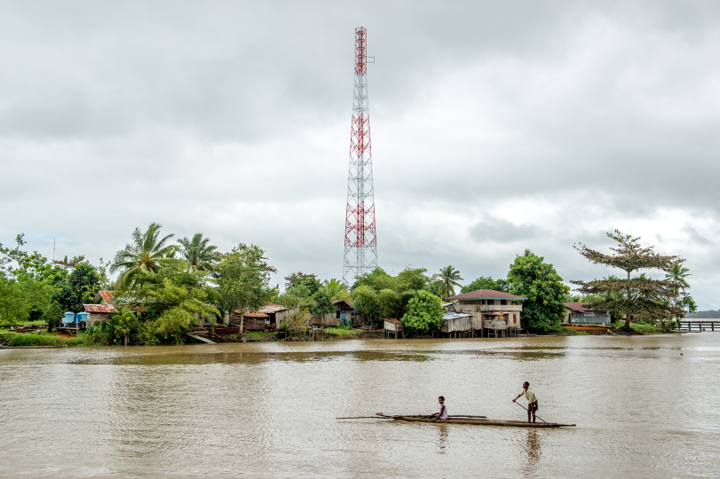 Boys rowing a longboat in front of one of three telephone towers that existed in Asmat in 2014.