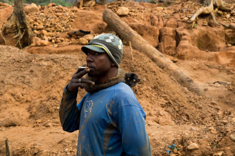 Diego Salimoali, age 37, stands with a pet brown lemur as he watches men work in the largest sapphire mining site in Bemainty, July 29, 2018. © Adriane Ohanesian